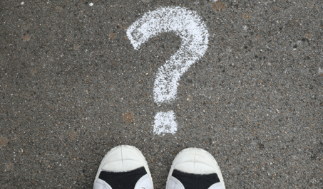 Top down view of a person standing on asphalt in front of a large question mark drawn in white